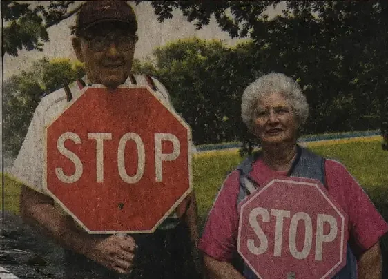 Christine Sandlin, 87, and her husband in their school crossing-guard vests, each holding a stop sign.